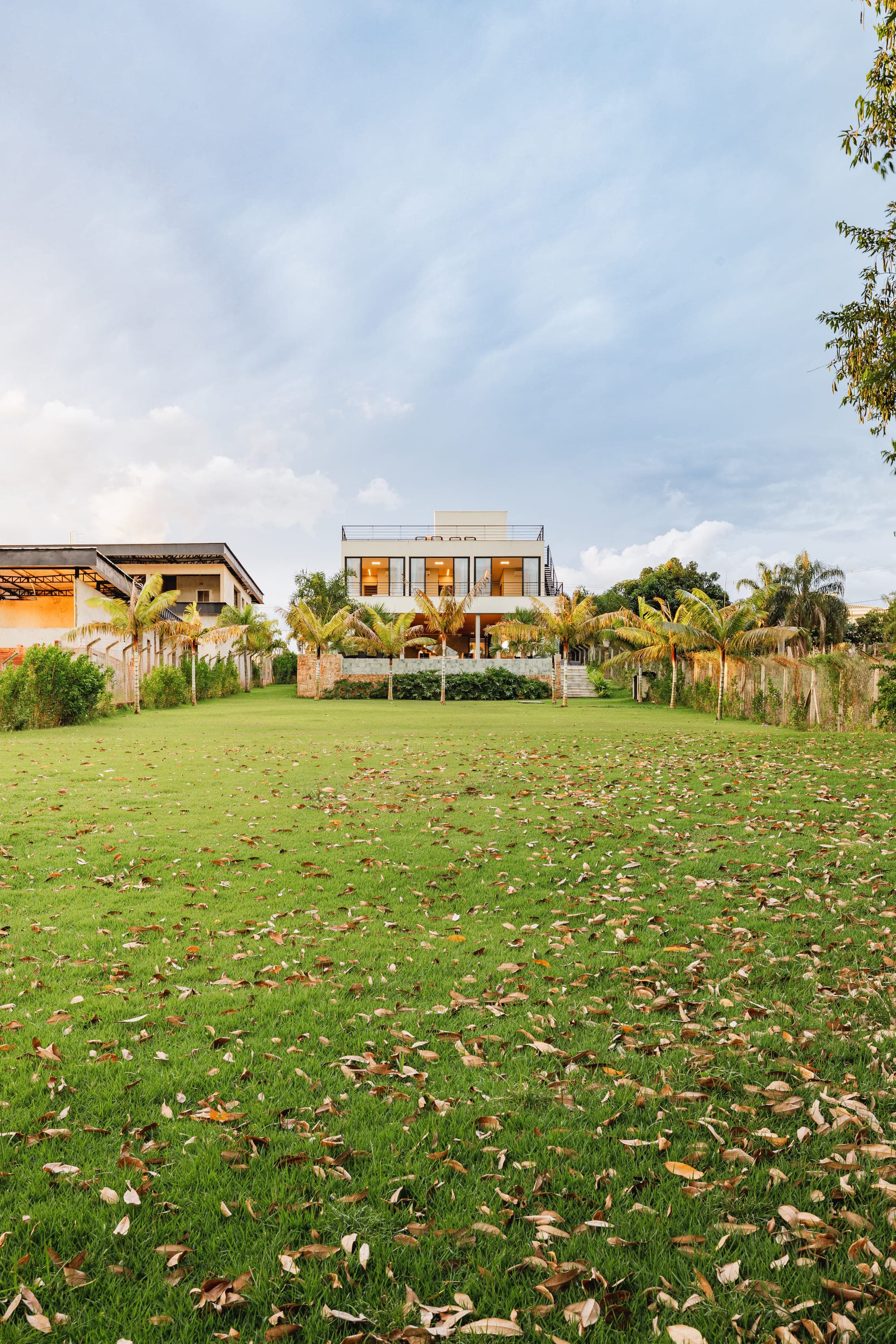 Casa vista de longe através do gramado, com folhas secas espalhadas no chão