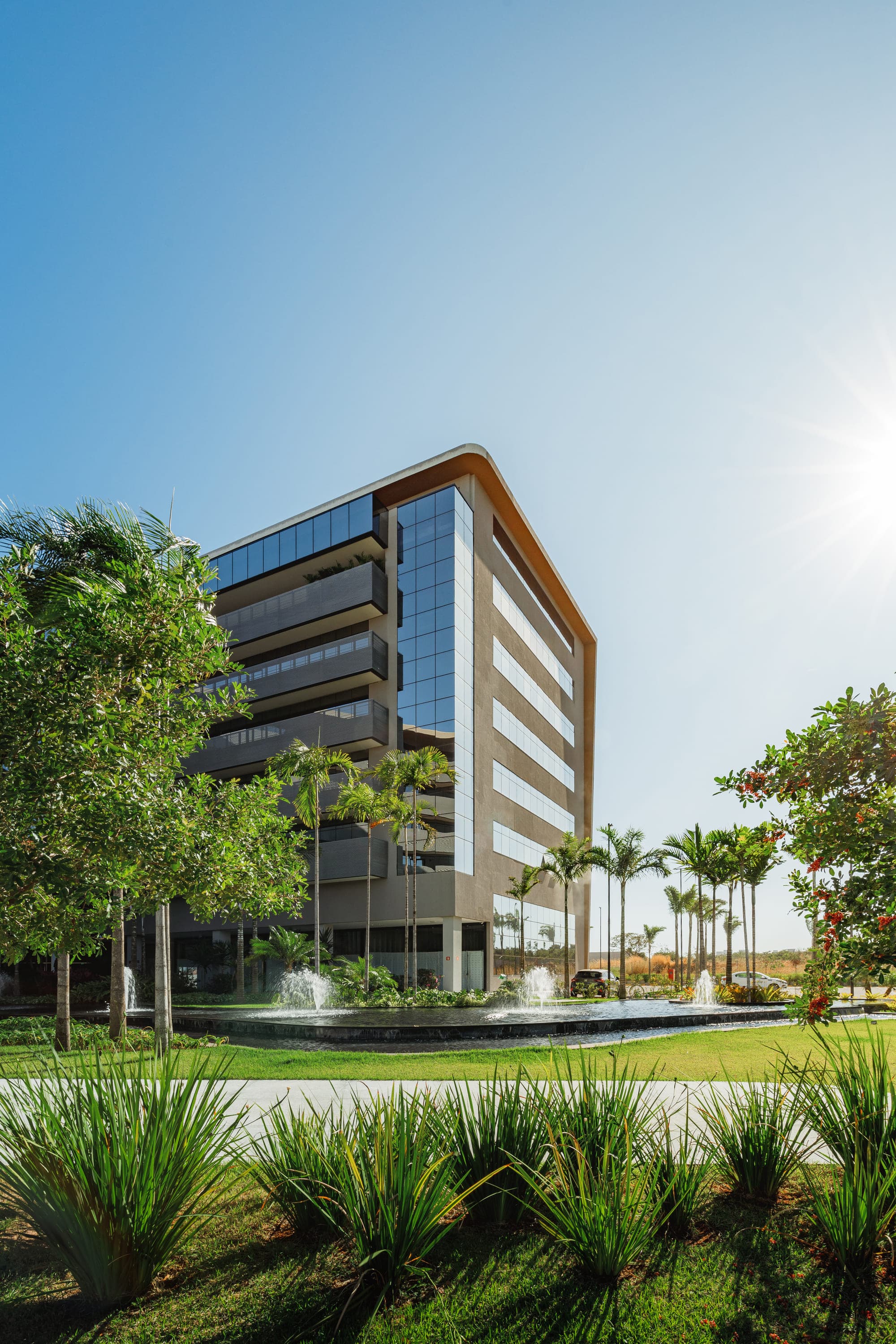 Edifício corporativo de vidro com espelho de água, palmeiras e jardim na entrada