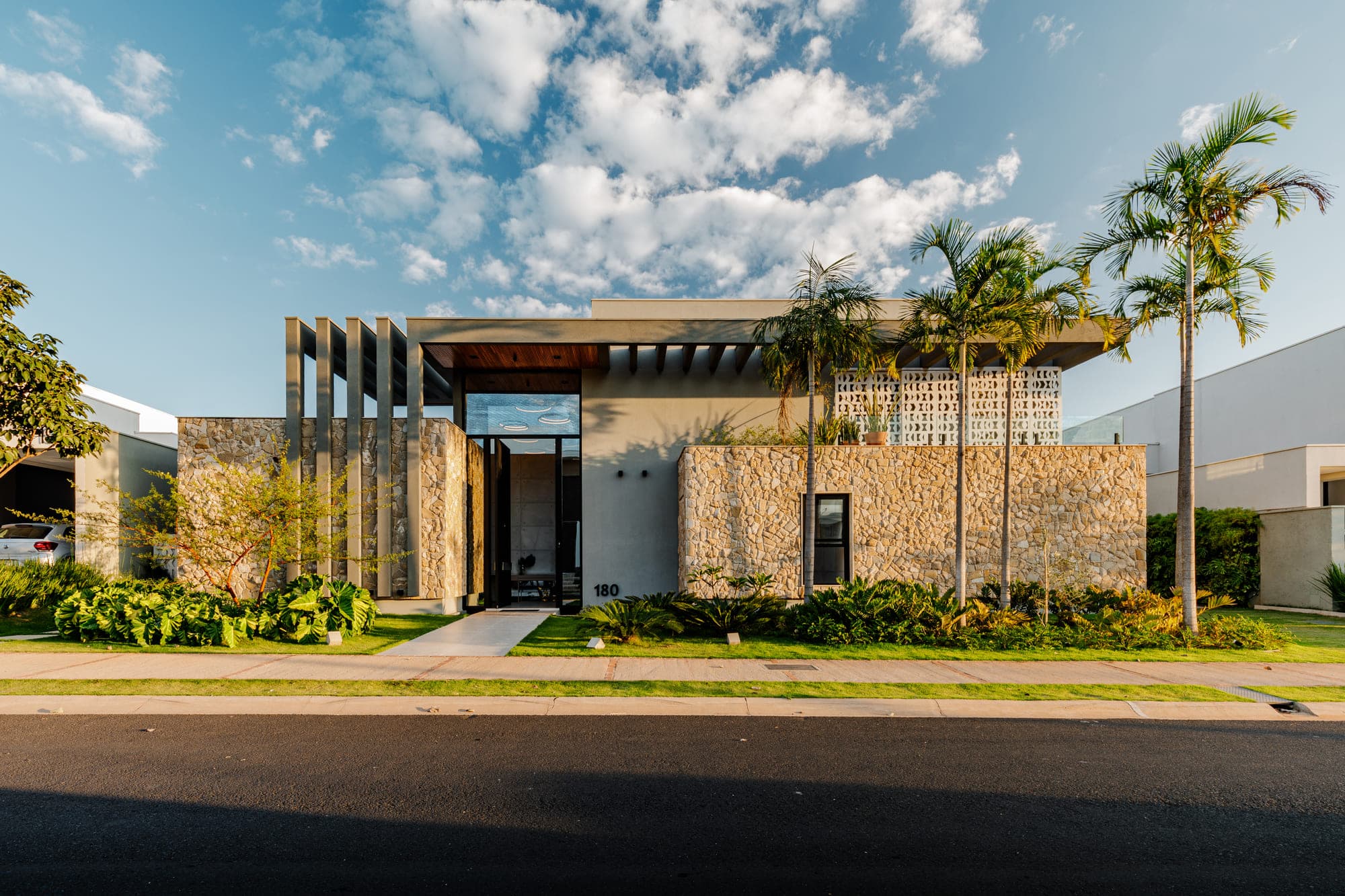 Fachada de casa com brises verticais de madeira, muro de pedra e jardim frontal