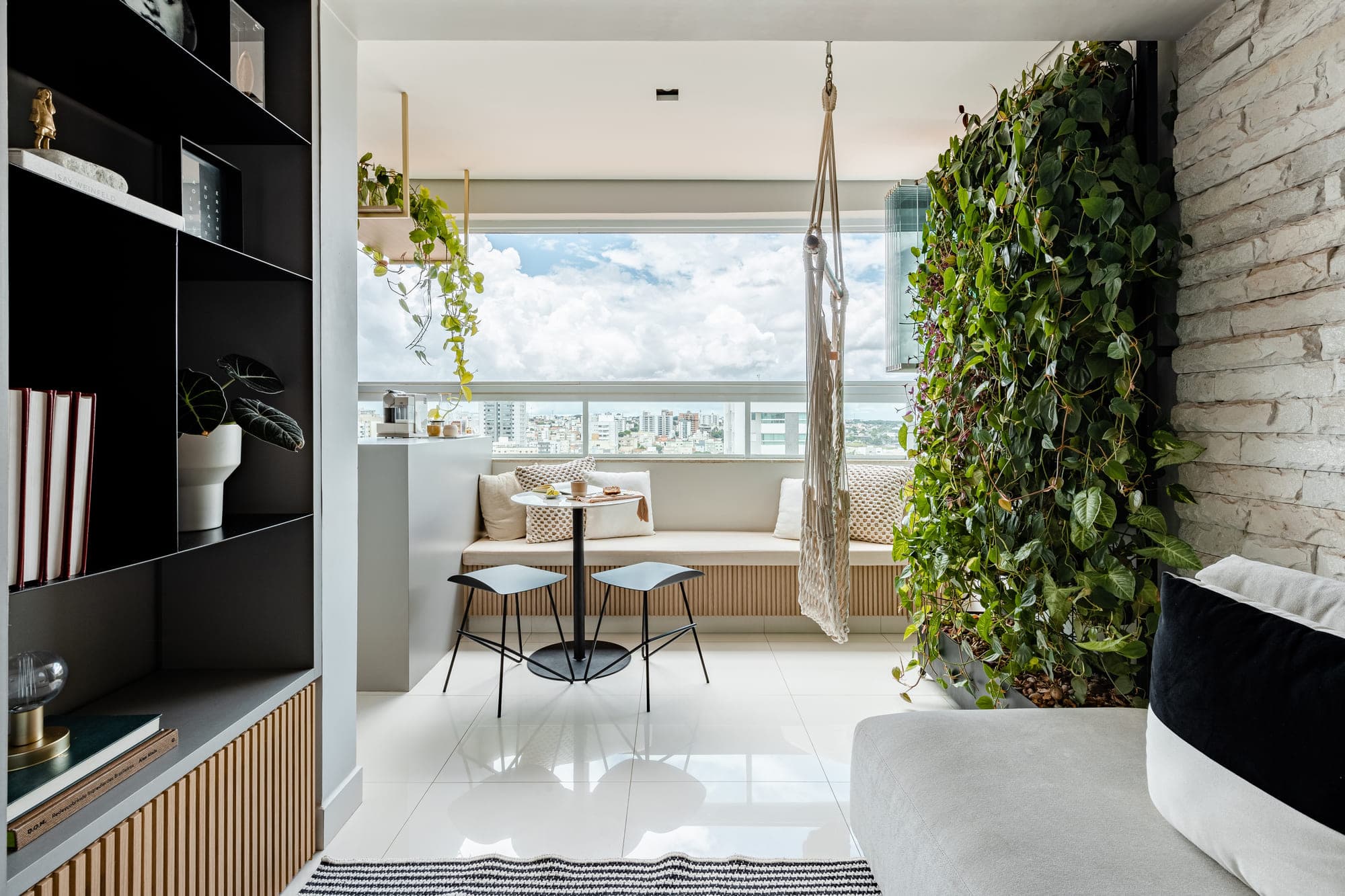 Varanda de apartamento com jardim vertical, mesa de café e vista para a cidade