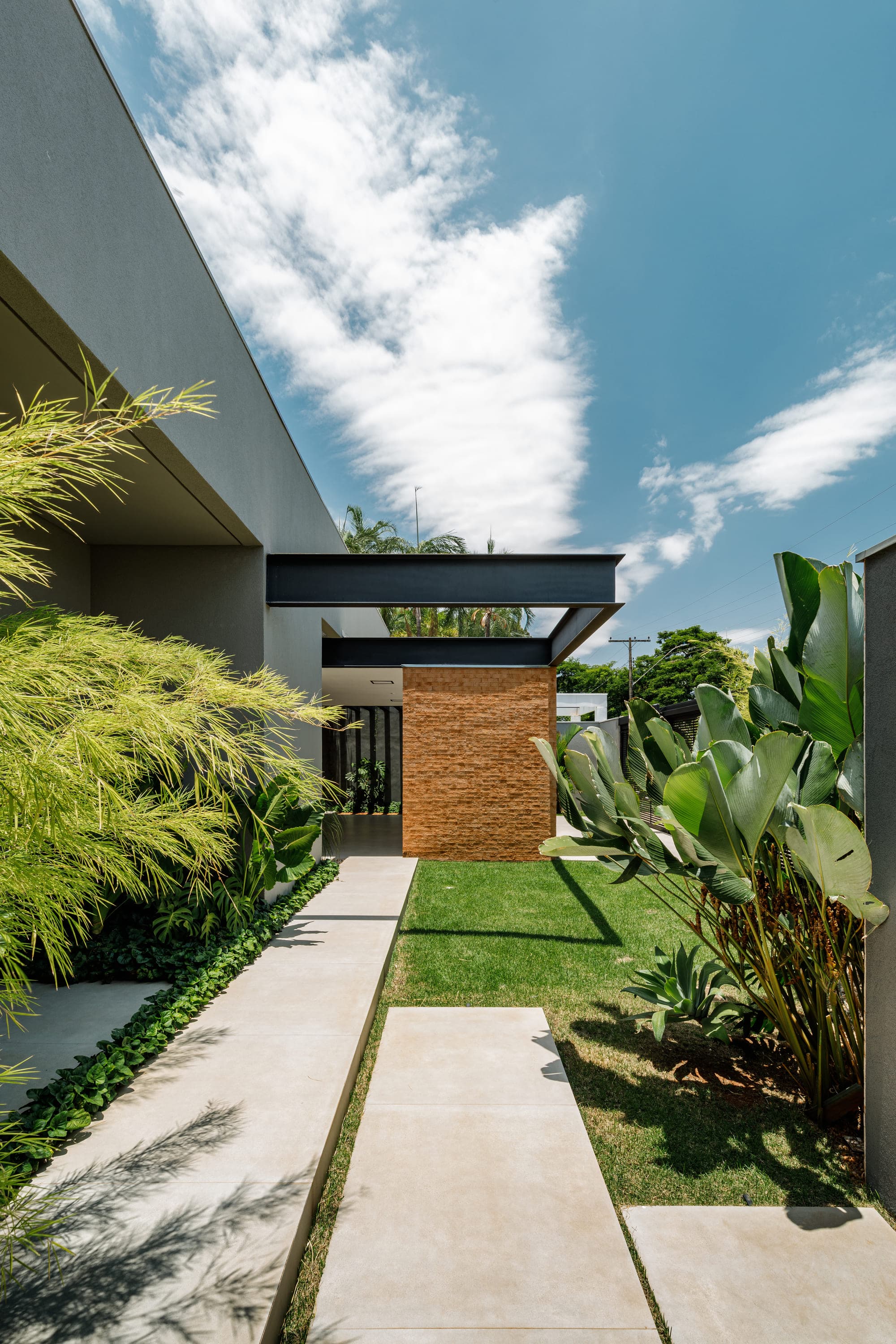 Fachada de casa com marquise, painel de madeira e vegetação densa em primeiro plano