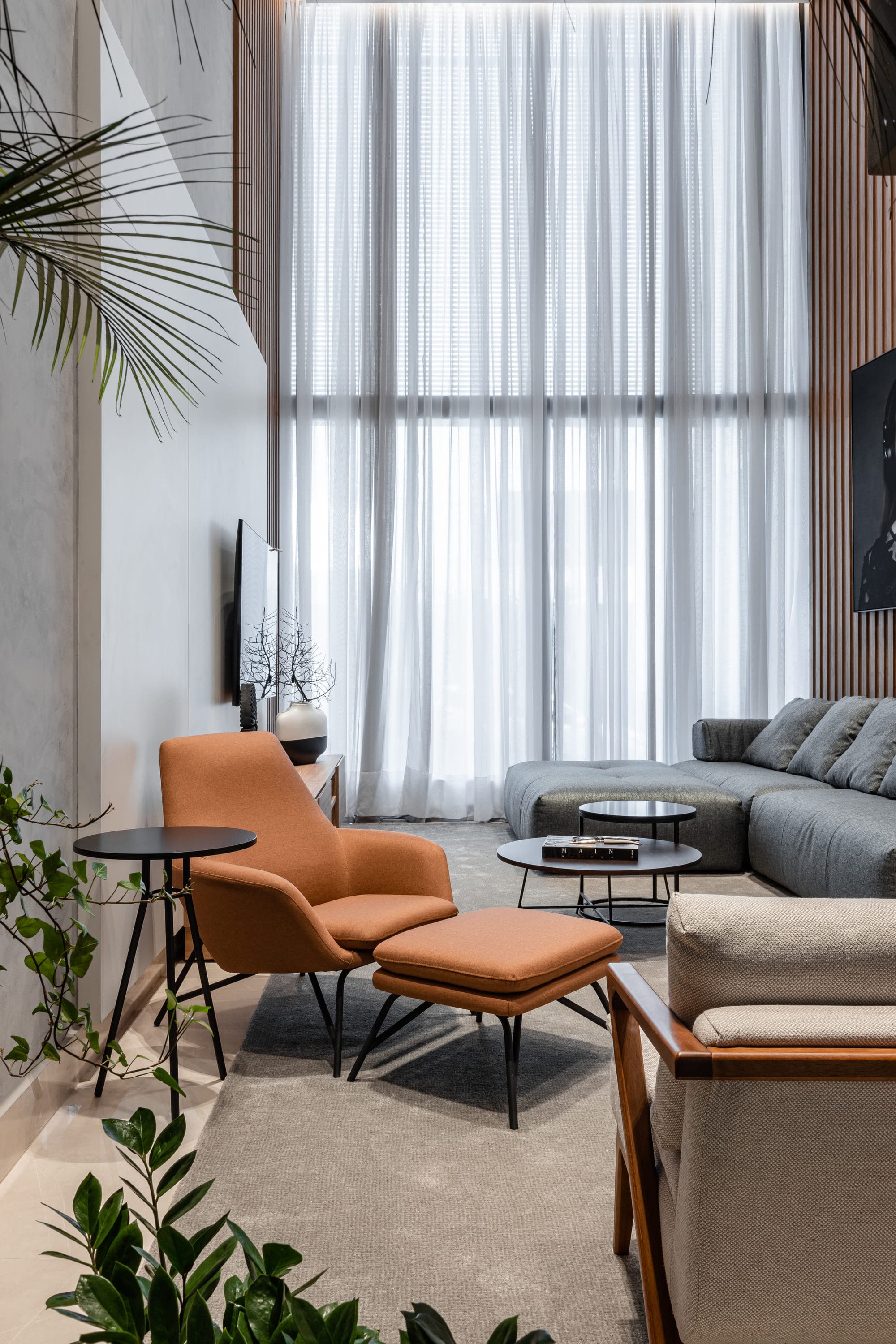 Sala de estar com cortina clara, poltrona de couro caramelo e sofá cinza