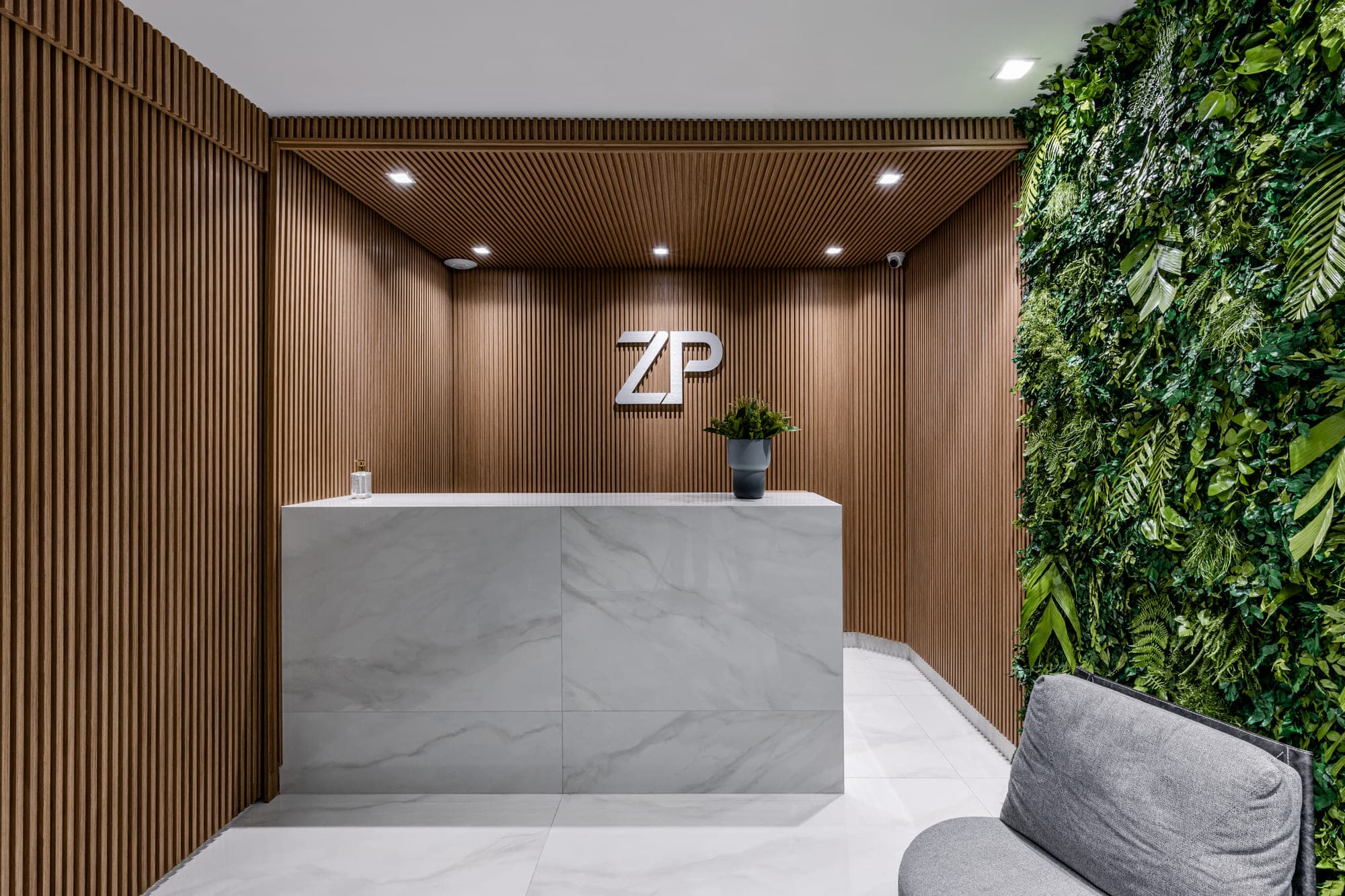 Recepção corporativa com balcão de mármore, painel ripado iluminado e jardim vertical
