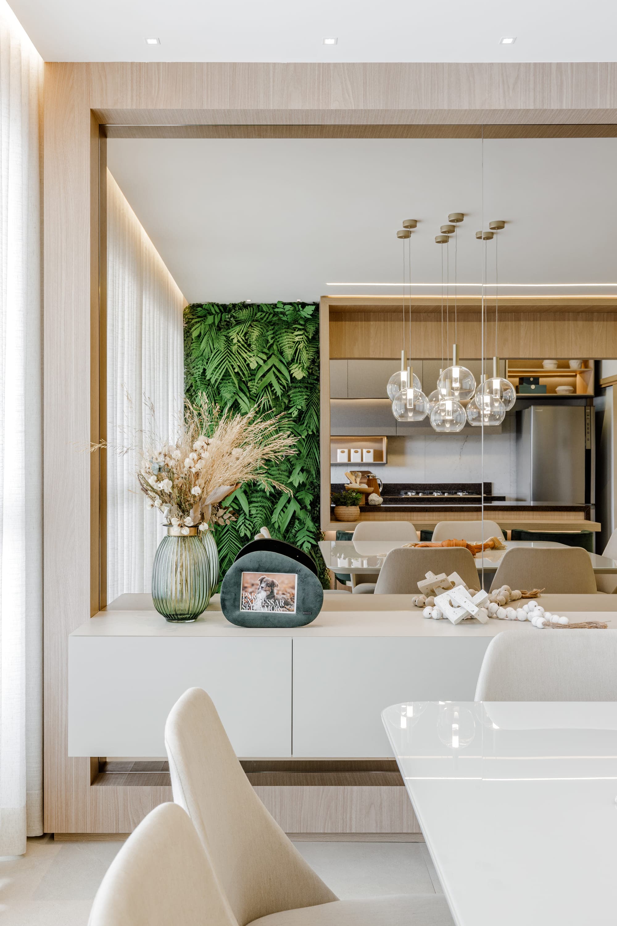 Cozinha integrada com bancada branca, jardim vertical e pendentes de vidro