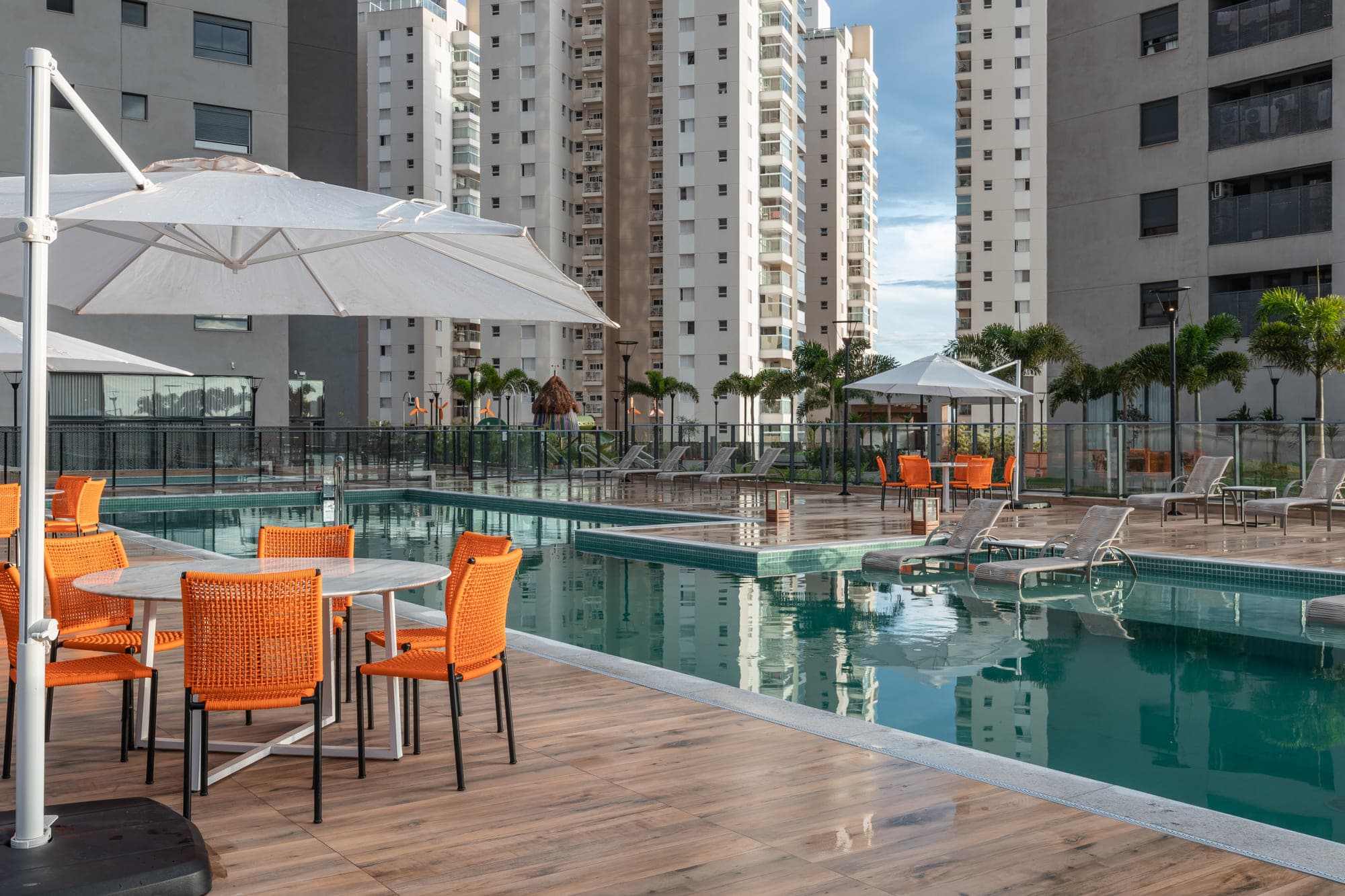 Área de lazer de condomínio com piscina, ombrelones e as torres ao fundo